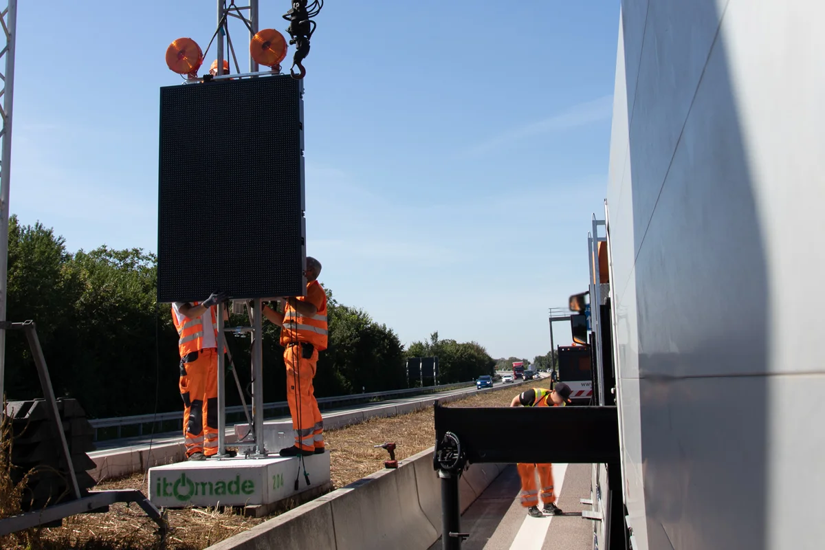 Monteure installieren eine LED-Stauwarnanlage auf IBOMADE-Betonfundament an der A656 bei Mannheim-Friedrichsfeld